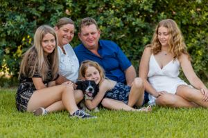 A group sits casually on grass with their pet dog during a sunny outdoor photoshoot.