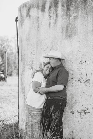 A couple shares an intimate moment against a weathered wall in black and white photography.