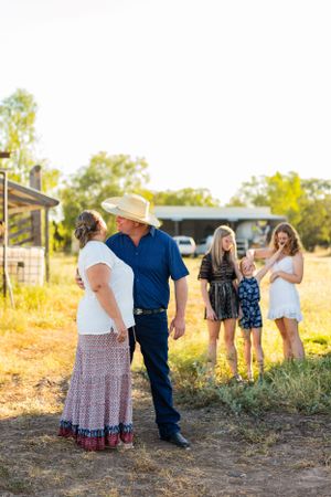 A couple stands together while others chat in the background of a rural setting.