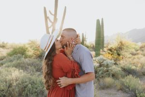 Intimate desert photoshoot with couple kissing among towering saguaro cacti at sunset.