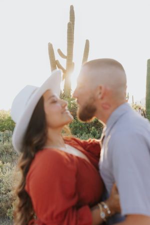 Romantic couple embracing in front of saguaro cactus during golden hour in the desert.