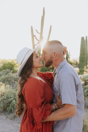 Couple sharing tender moment in red dress and casual attire against desert landscape.