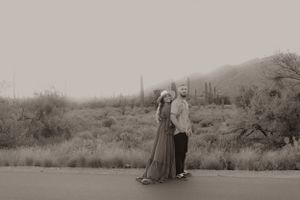 A black and white desert landscape photo with two people posing on a road.
