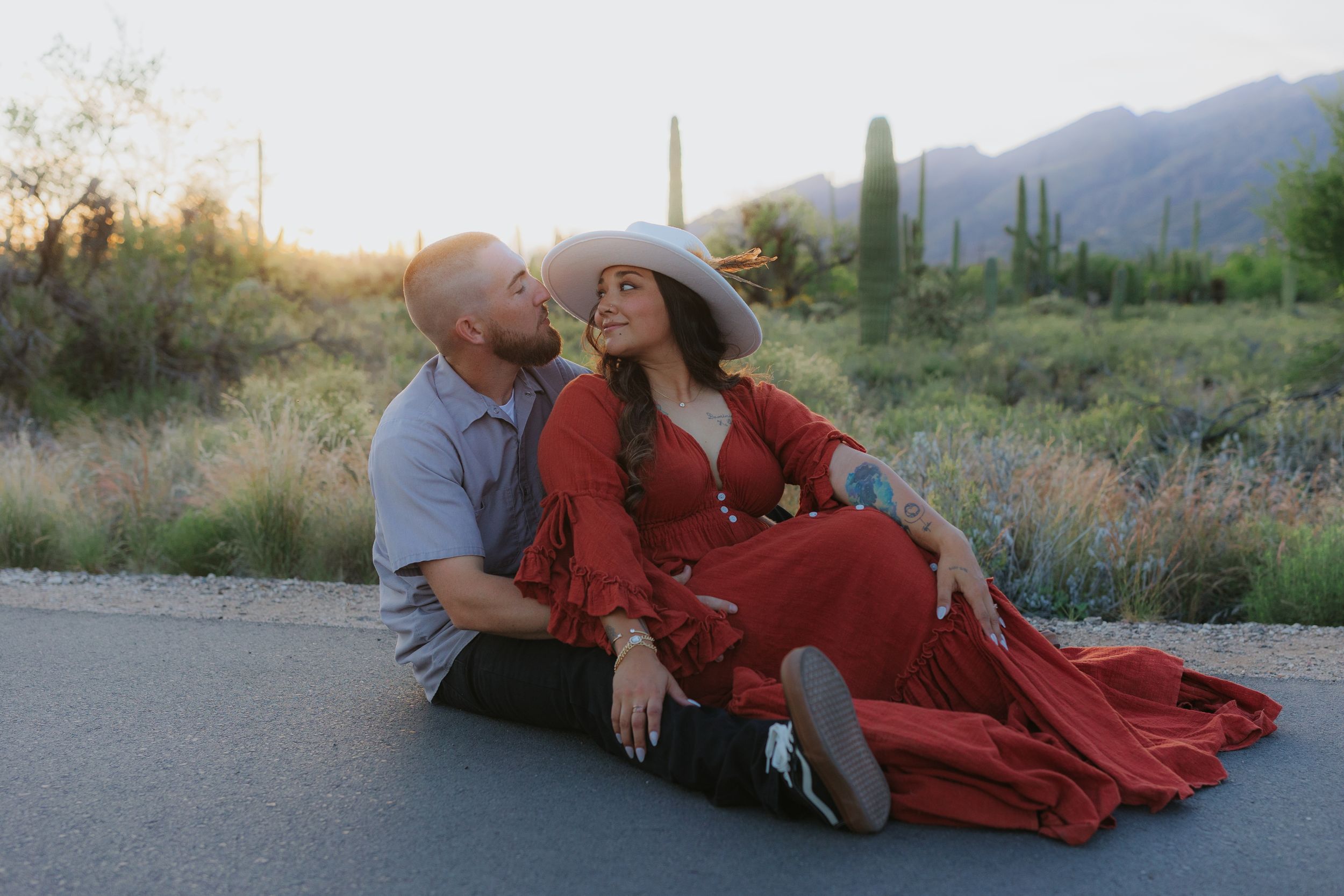 A couple poses together on the ground during a sunset desert photoshoot.