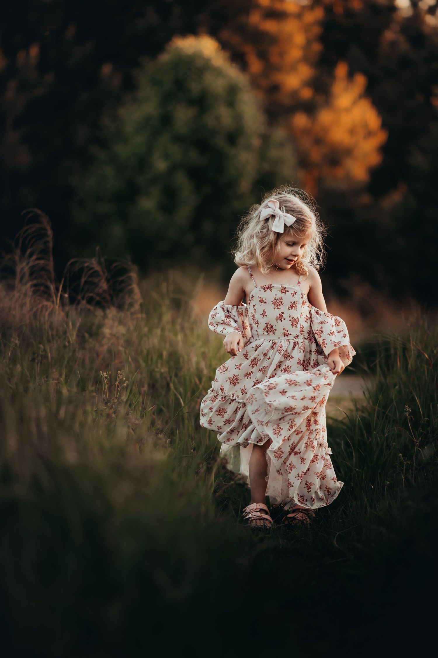 Little 4yo girl with blonde curly hair spins in a Joyfolie dress in grass at sunset for milestone session.