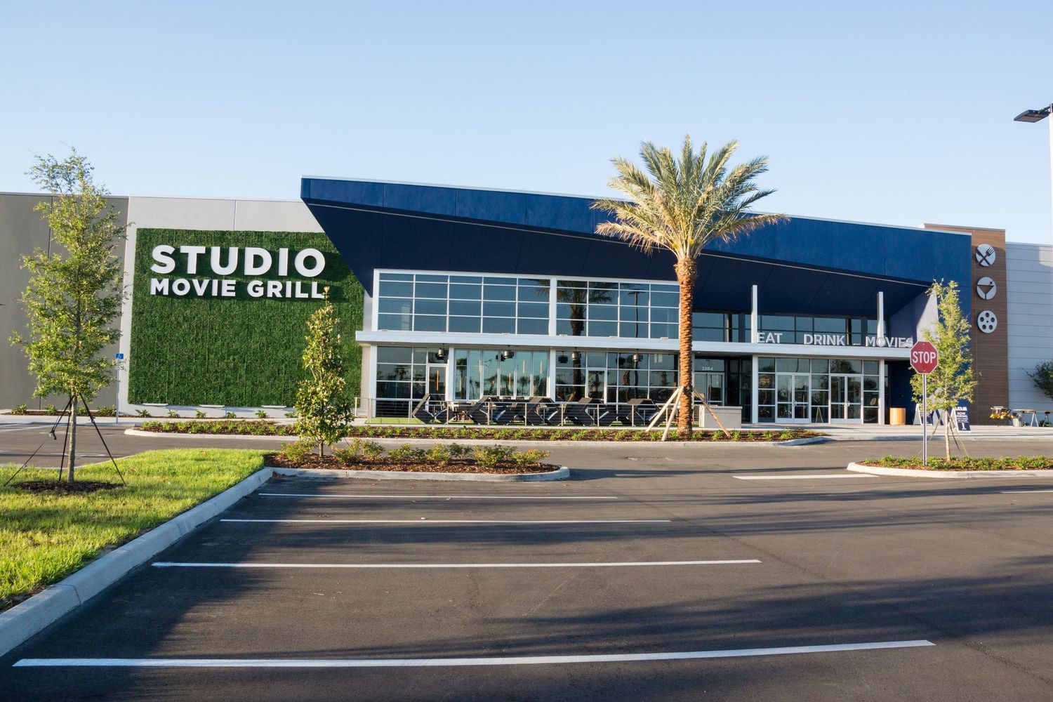 Modern retail building exterior with Studio Movie Grill signage and palm trees in parking lot.