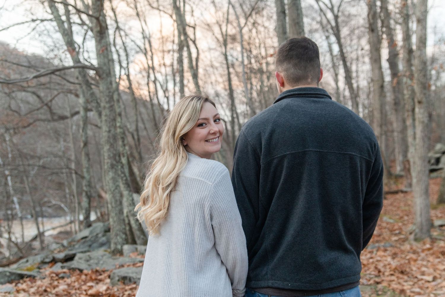 Casual engagement photo of couple in sweaters among fall foliage.