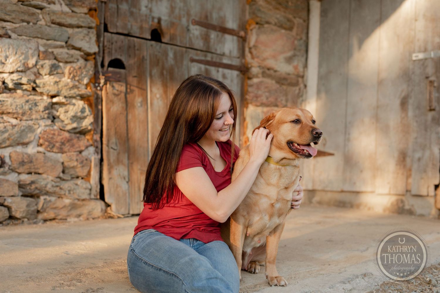 Person in red top playing with happy golden retriever dog by stone building.