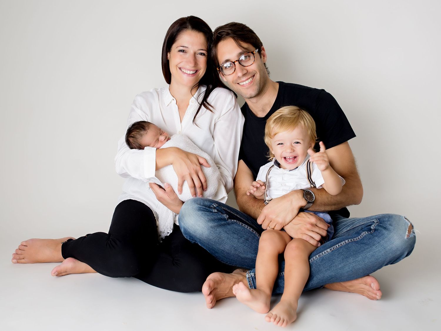 Happy family with two small children sitting together on white background for portrait session.