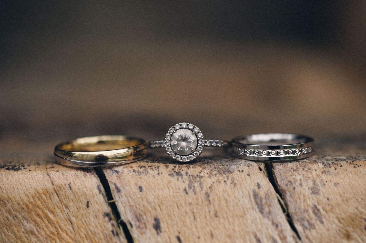 Three wedding rings arranged on rustic wooden surface with diamond engagement ring in center.