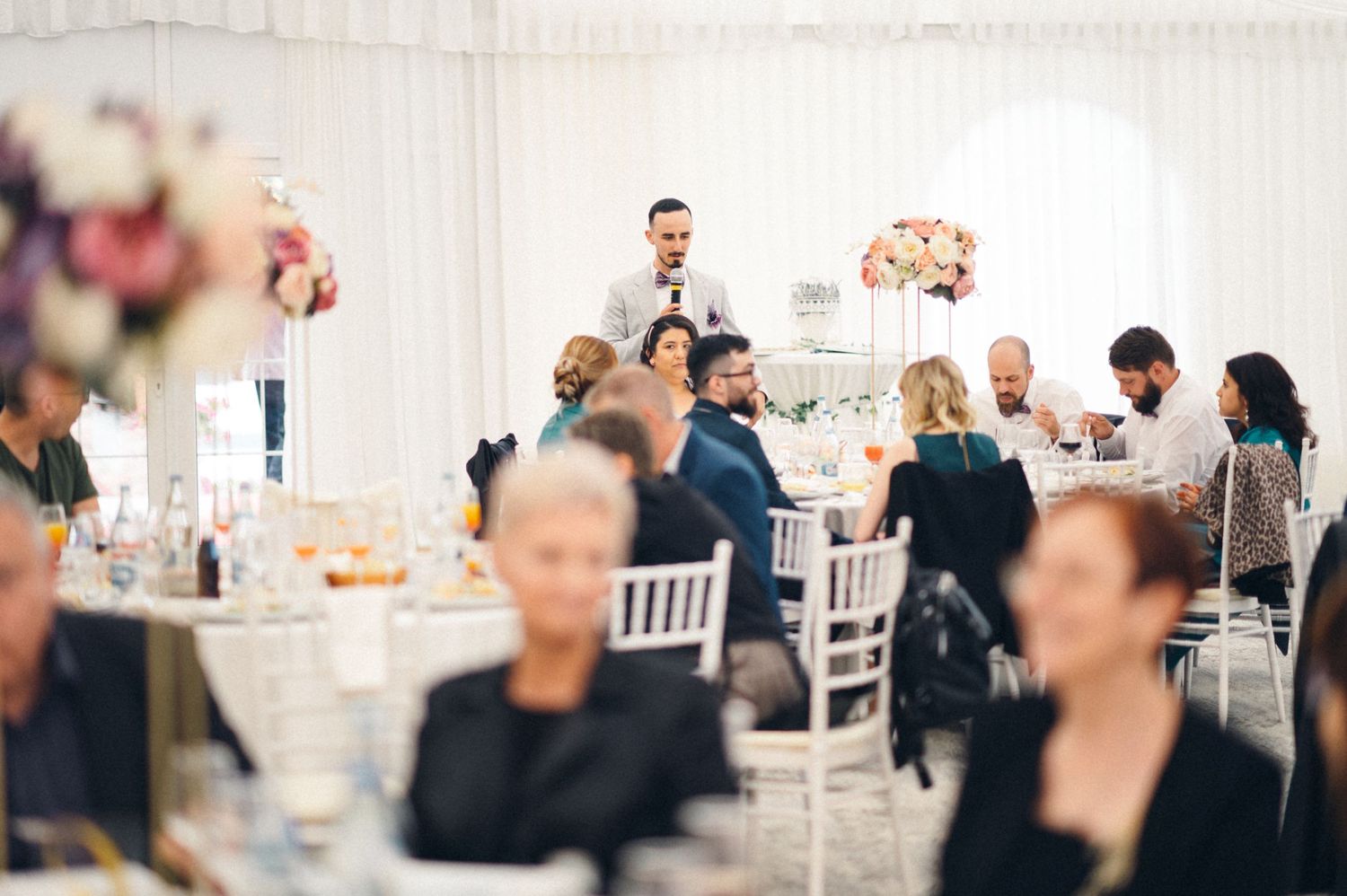Wedding reception in a white tent with decorated tables and guests enjoying the celebration.