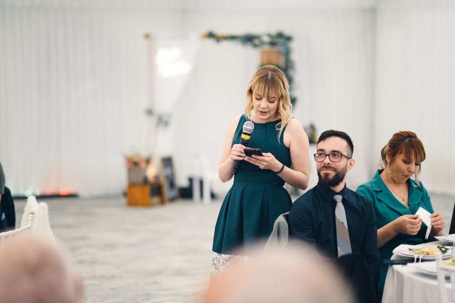 A guest in a navy dress checks their phone during an indoor wedding reception.