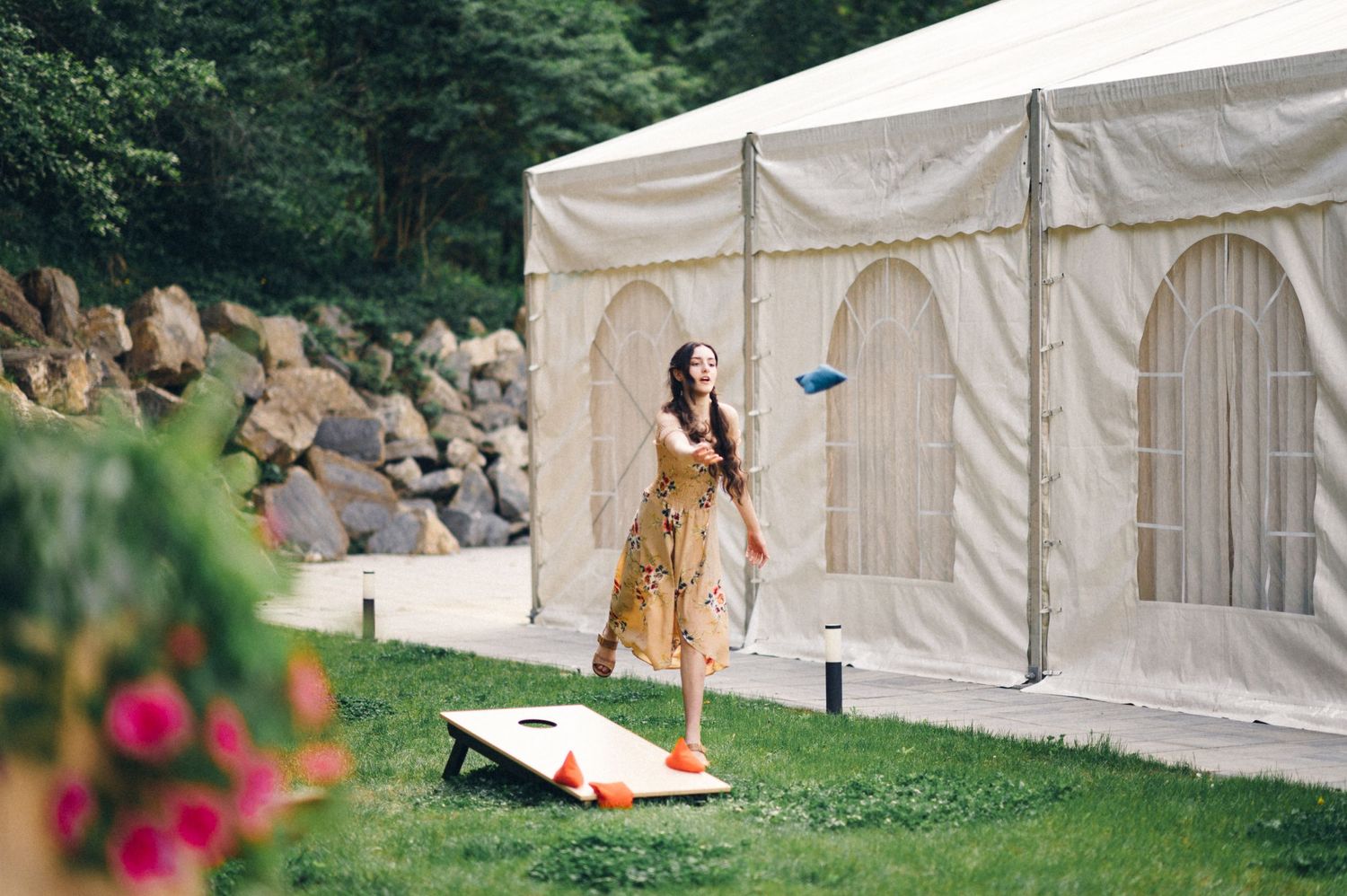 Person playing cornhole game outside white event tent on sunny summer day.