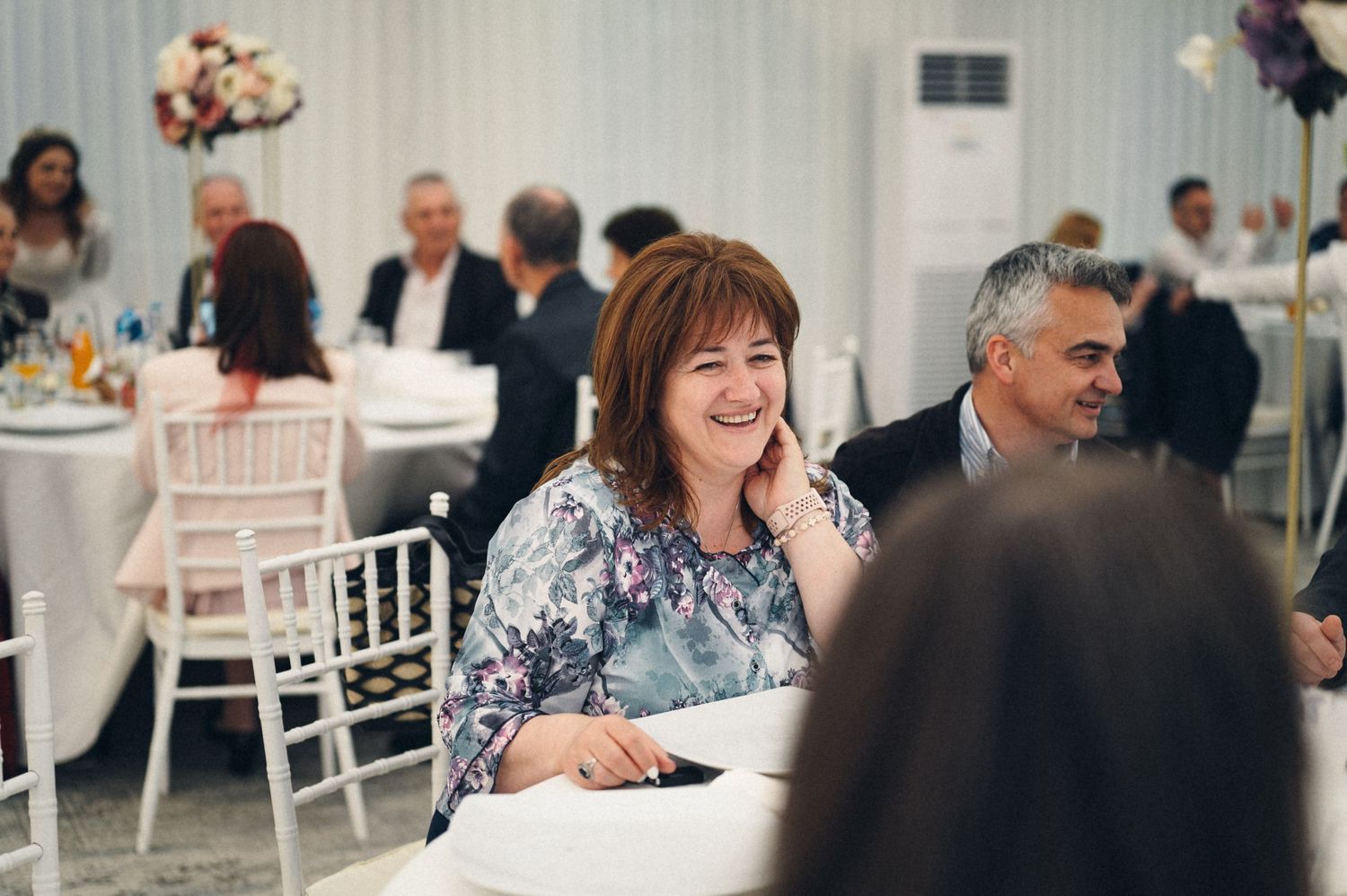 Wedding reception guests enjoying conversation at decorated white tables.