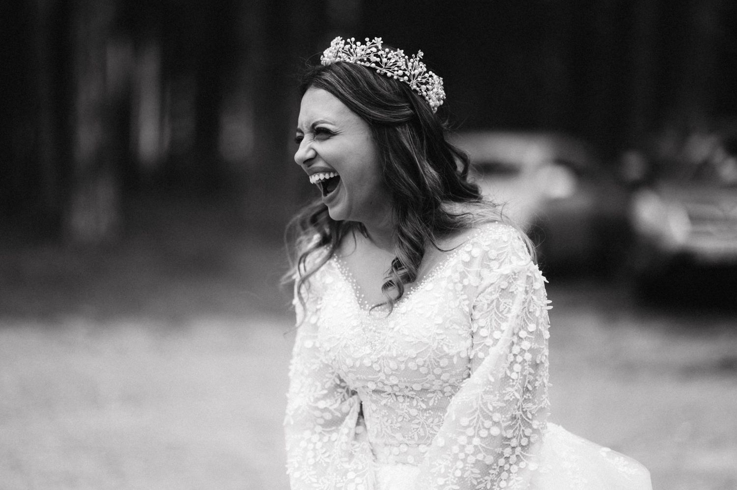 Black and white portrait of joyful bride wearing lace dress and crystal crown.
