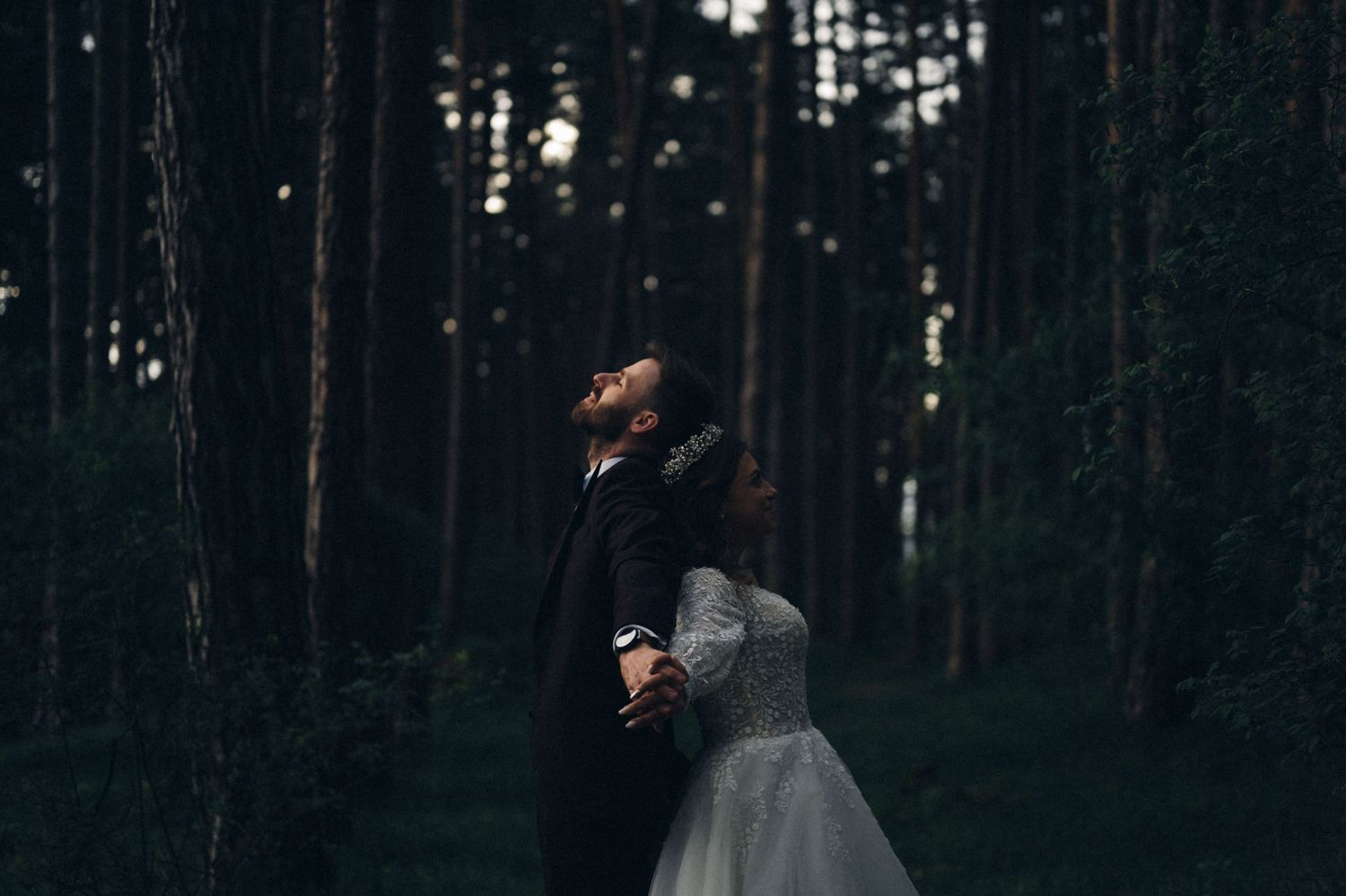 Silhouette of bride and groom holding hands in dark forest.