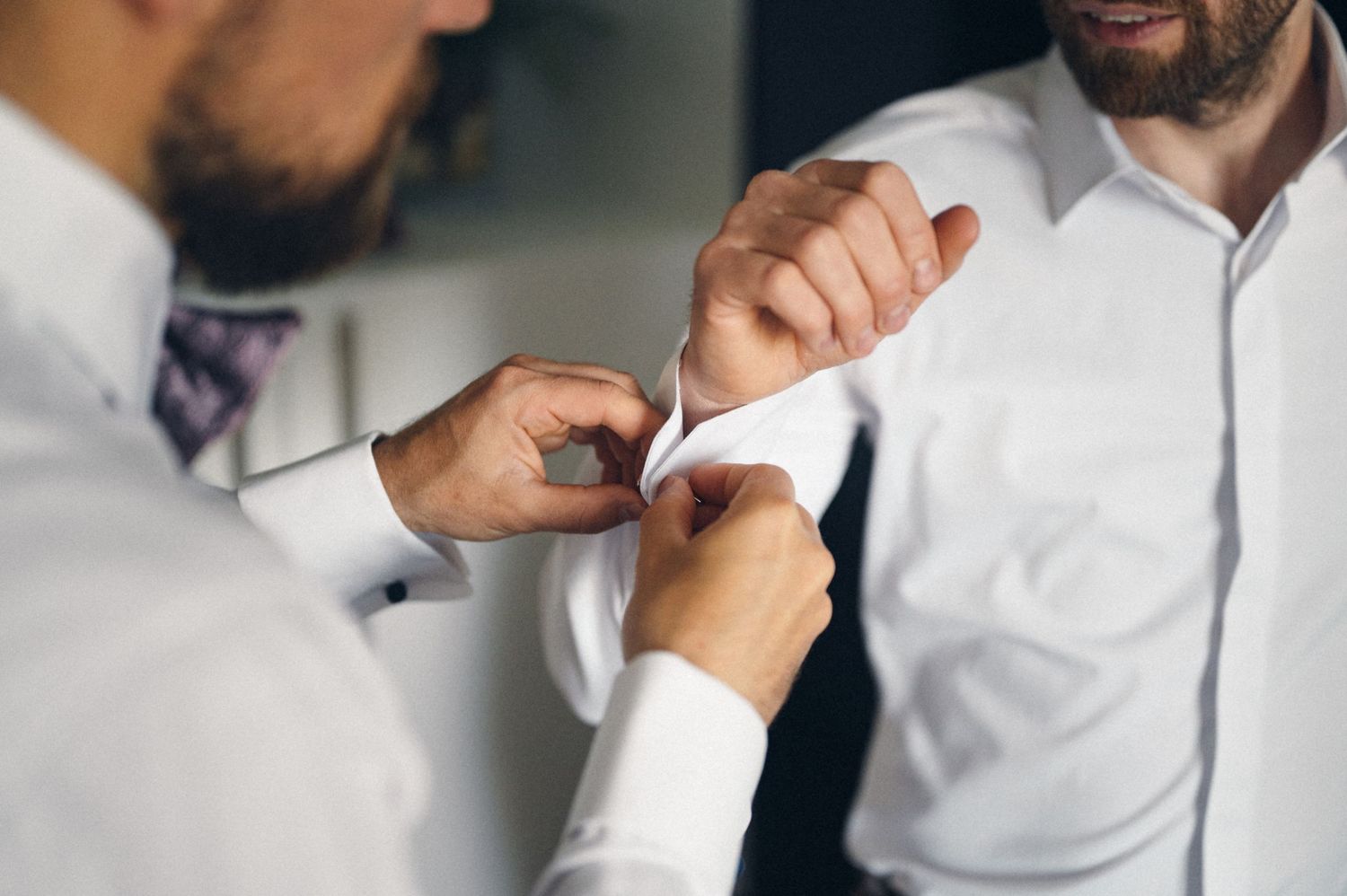 Close-up of hands adjusting formal white shirt buttons during wedding preparation.