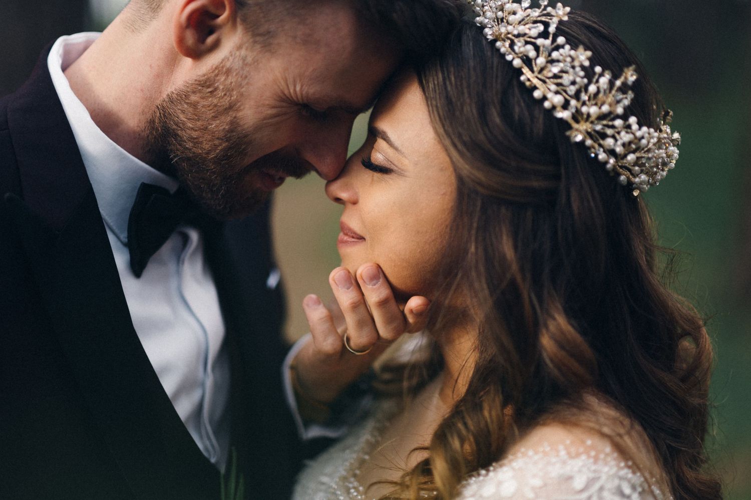 Intimate close-up of wedding couple sharing tender moment with bride wearing crystal crown.