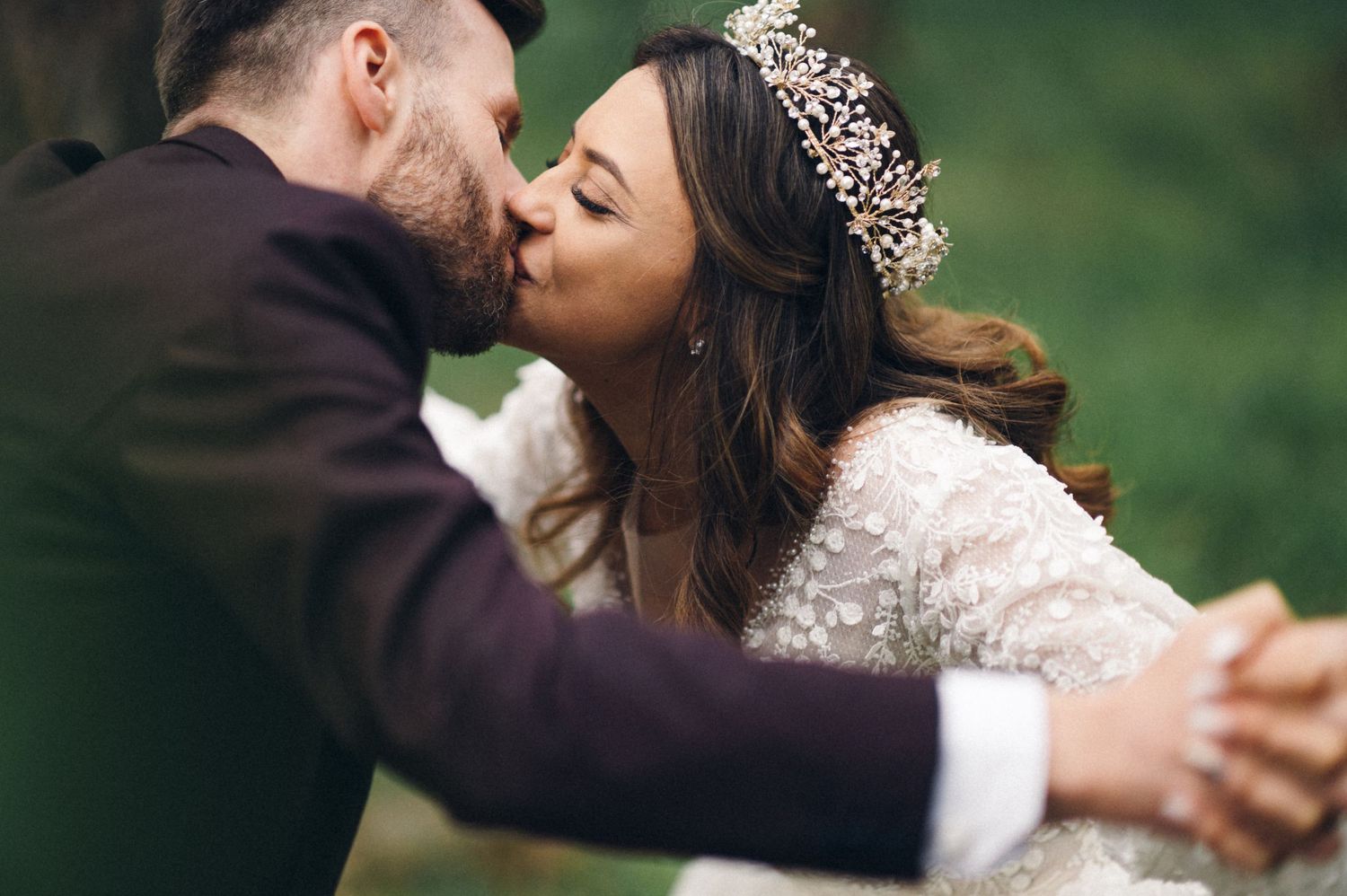 Romantic embrace between newlyweds in forest setting with bride in lace dress and crystal headpiece.