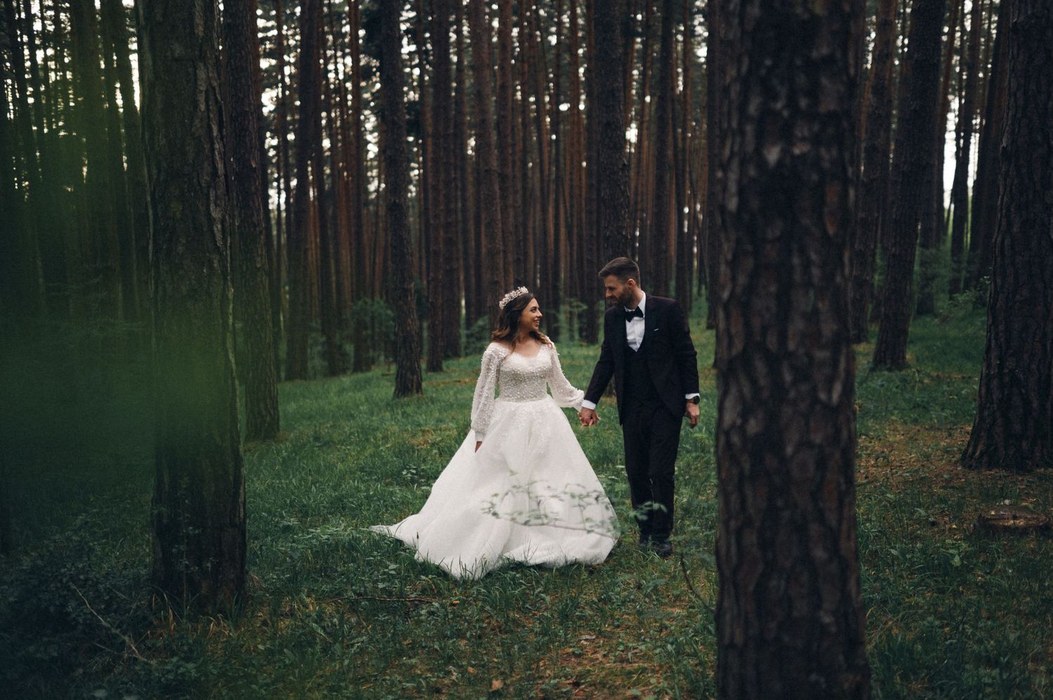 A couple shares a romantic moment among tall pine trees during their forest wedding.