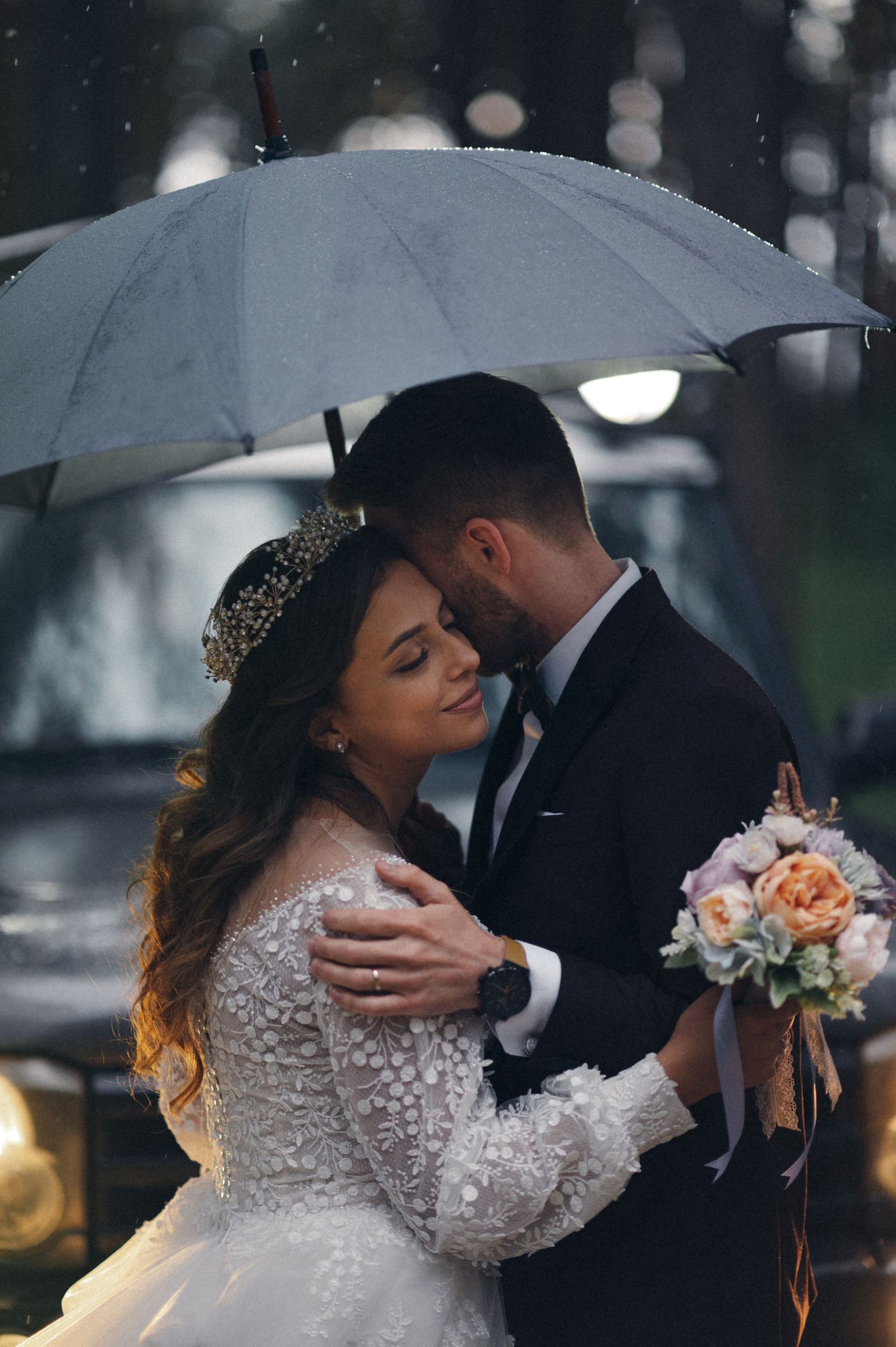 Romantic wedding portrait in the rain with soft bokeh lights and floral bouquet.