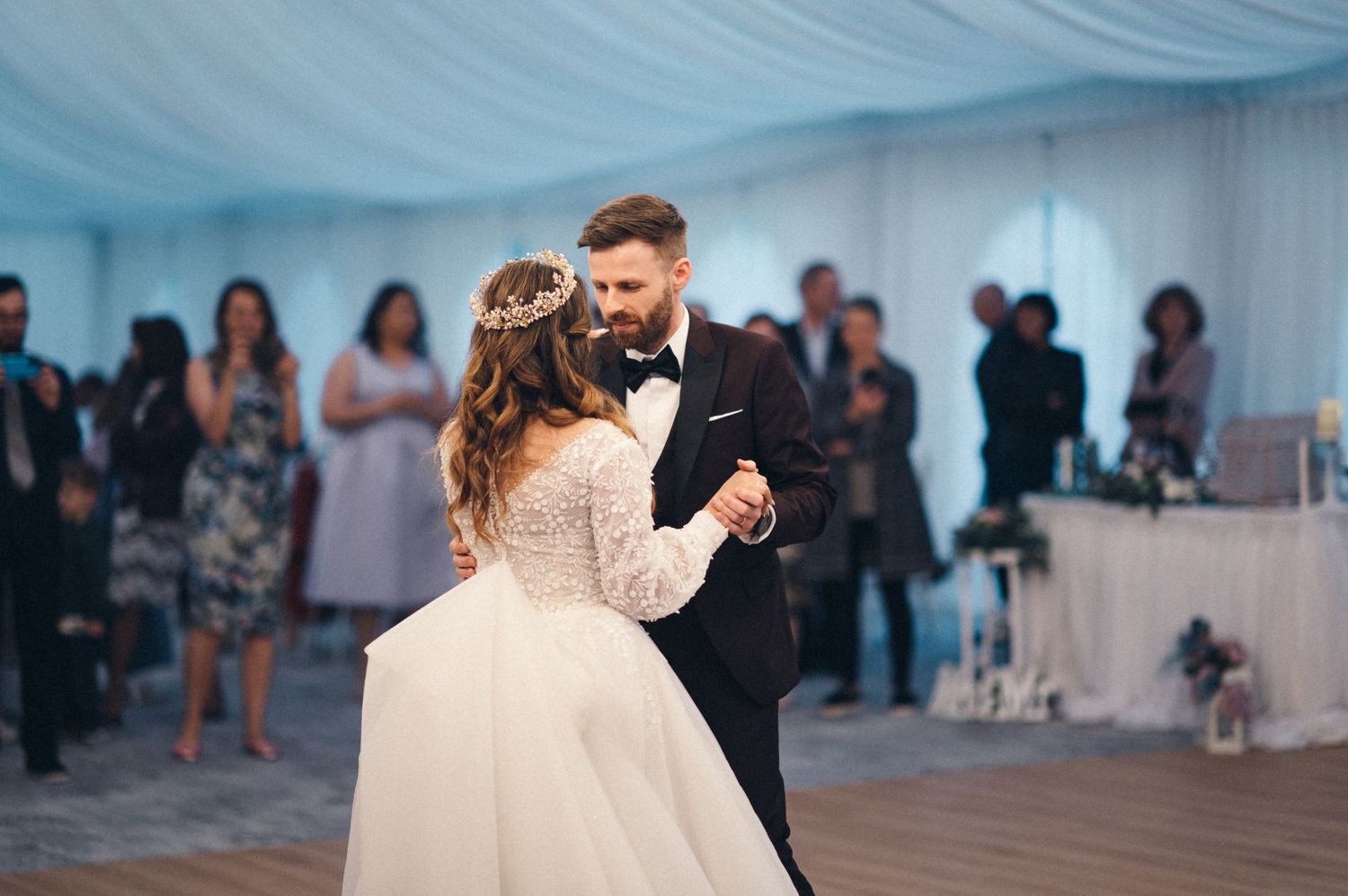 A couple dances elegantly on a wooden floor under a white draped tent ceiling at their wedding reception.
