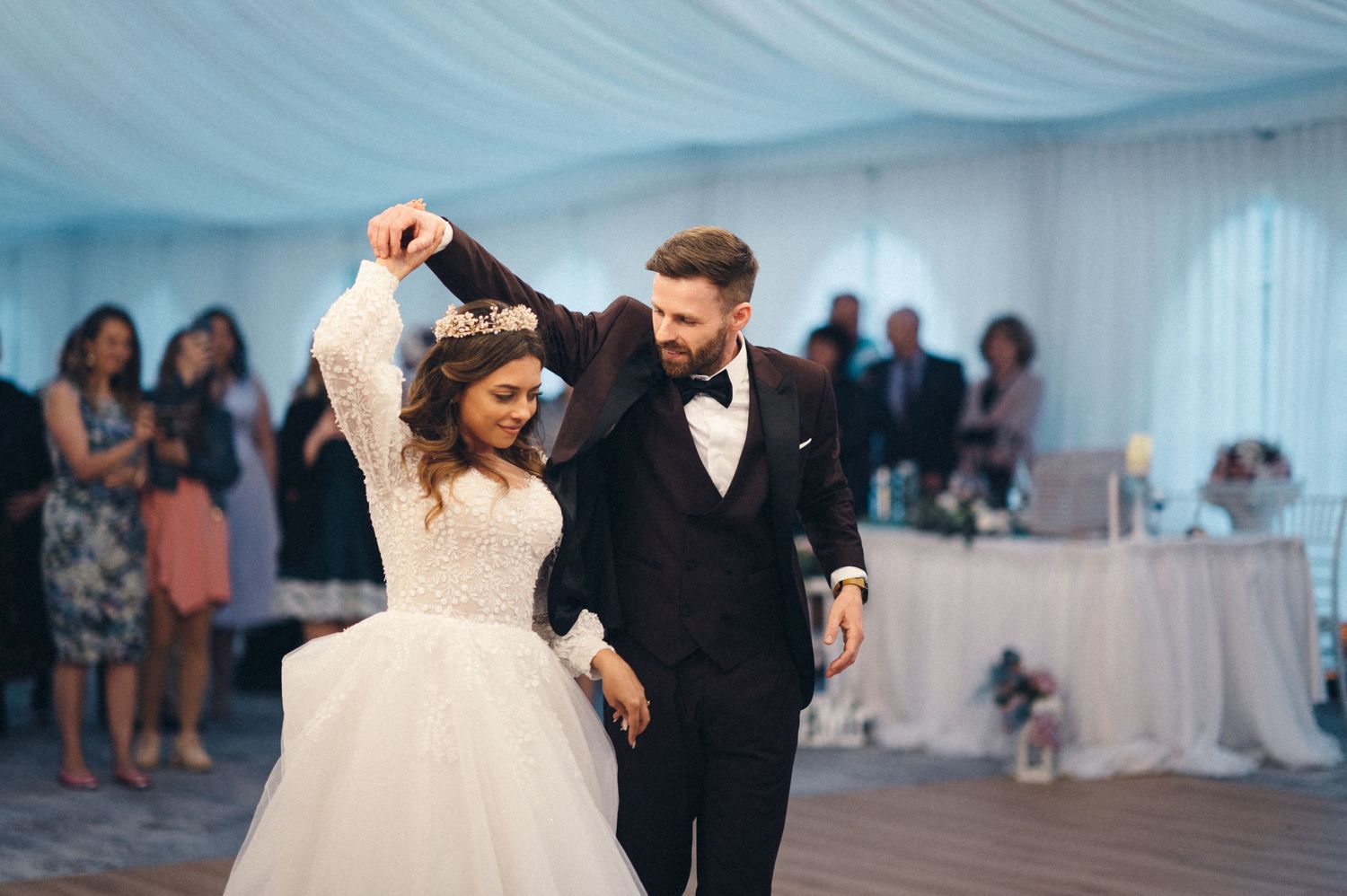 A couple performs a romantic dance move during their wedding reception under blue-tinted tent lighting.