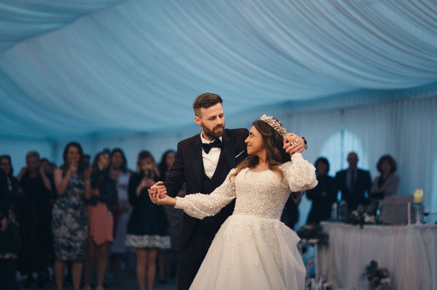 A couple shares an intimate dance moment under blue-tinted lighting at their wedding reception.