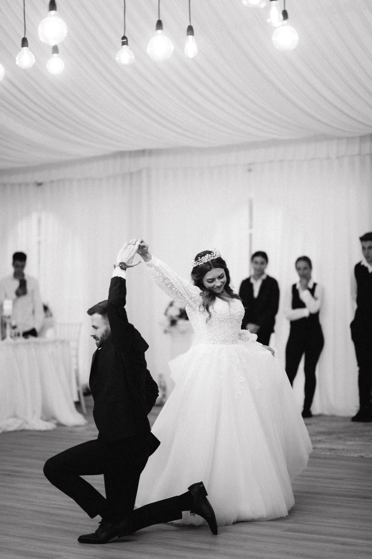 A dramatic black and white capture of a wedding dance with suspended light bulbs overhead.
