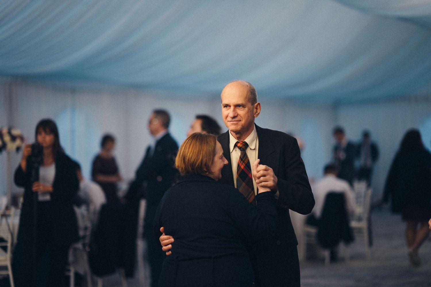 Guests dance and socialize at an elegant wedding reception under a draped tent ceiling.