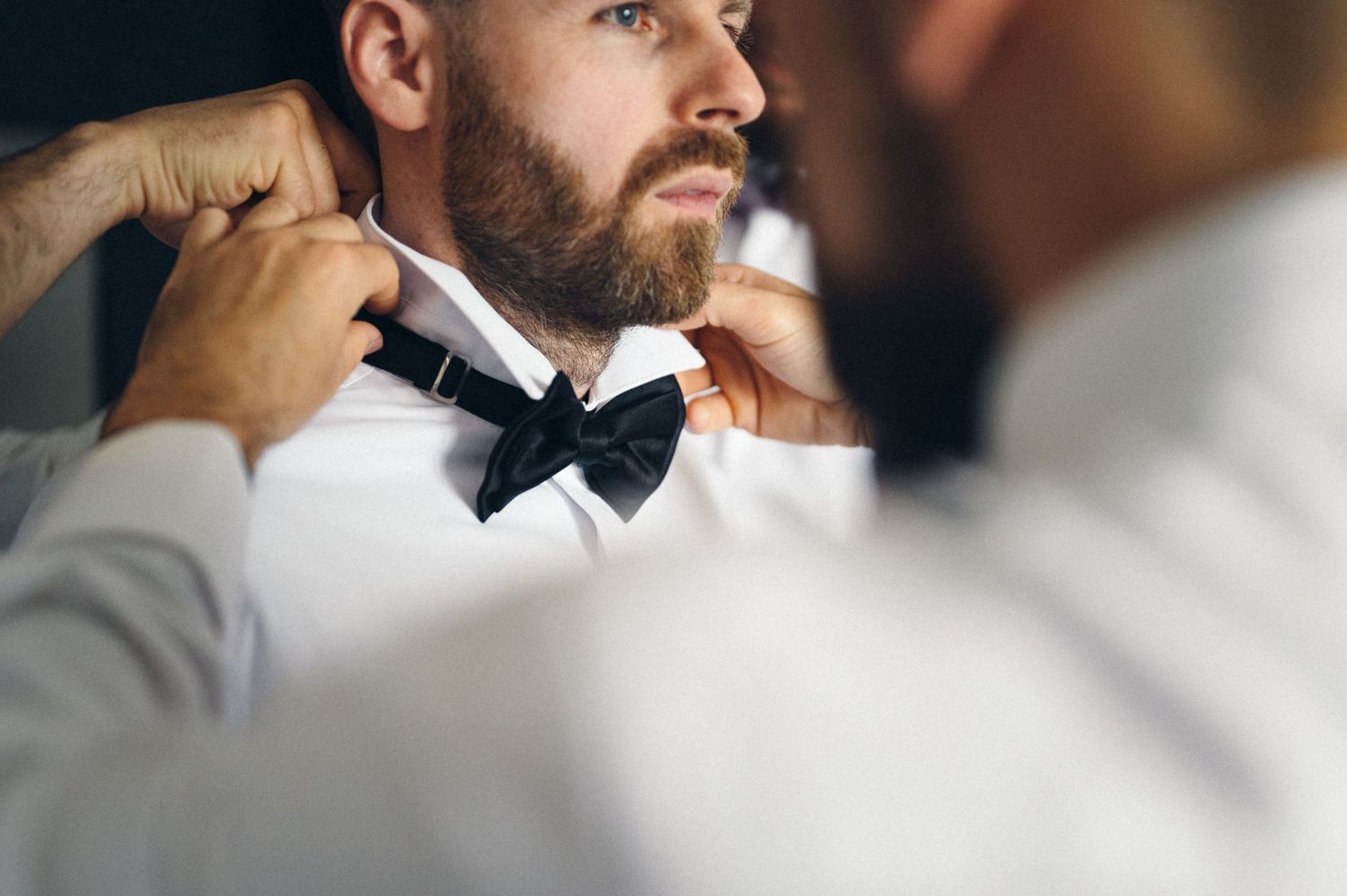 Hands adjusting a black bowtie on formal attire during wedding preparations.