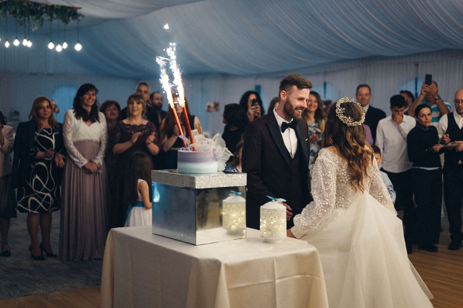 Newlyweds cut their wedding cake surrounded by sparklers and guests.