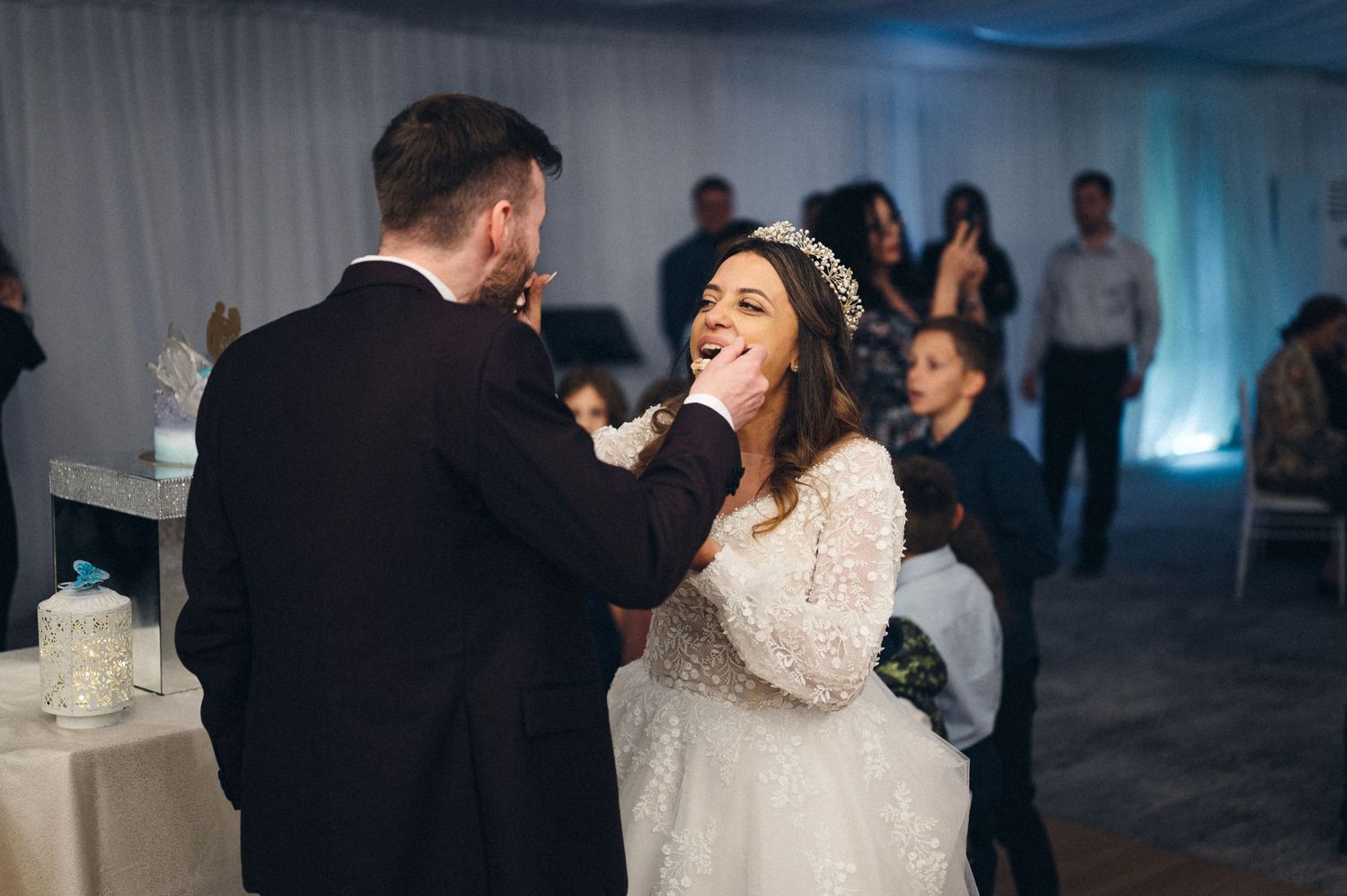 Happy couple feeds each other wedding cake during reception celebration.