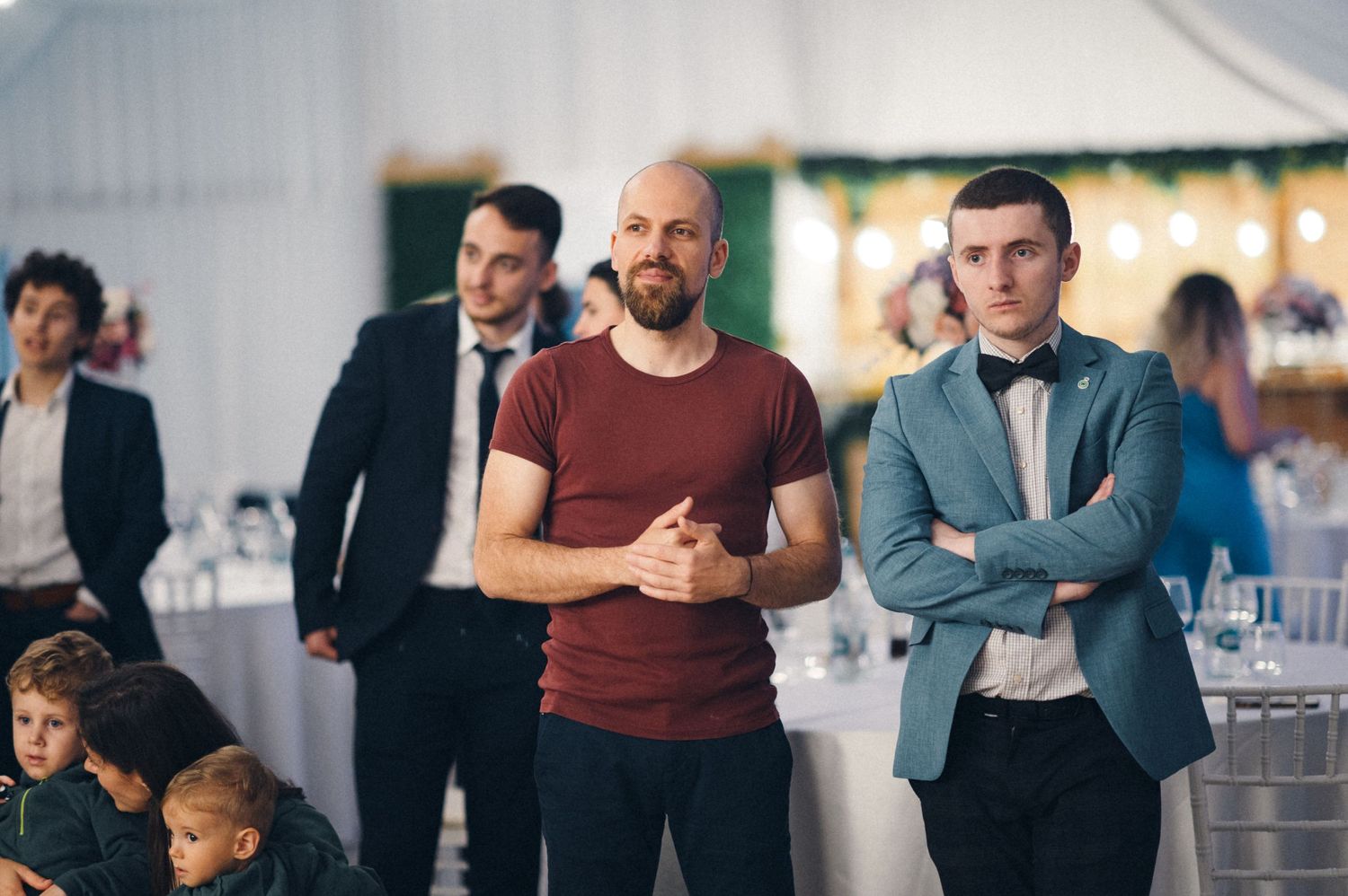 Wedding guests watch reception activities in formal attire.