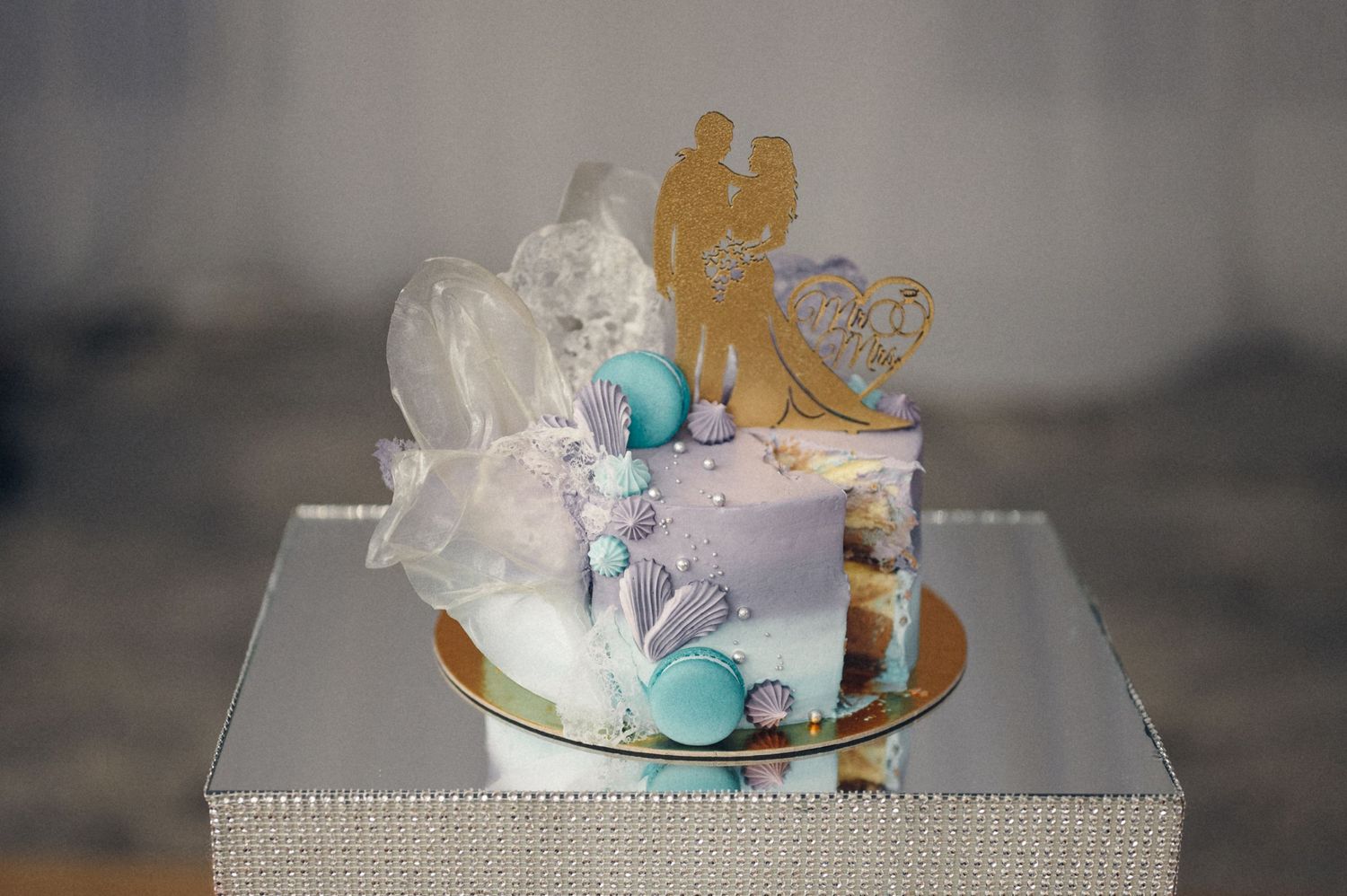 Wedding cake decorated with golden silhouettes and blue accents on silver stand.