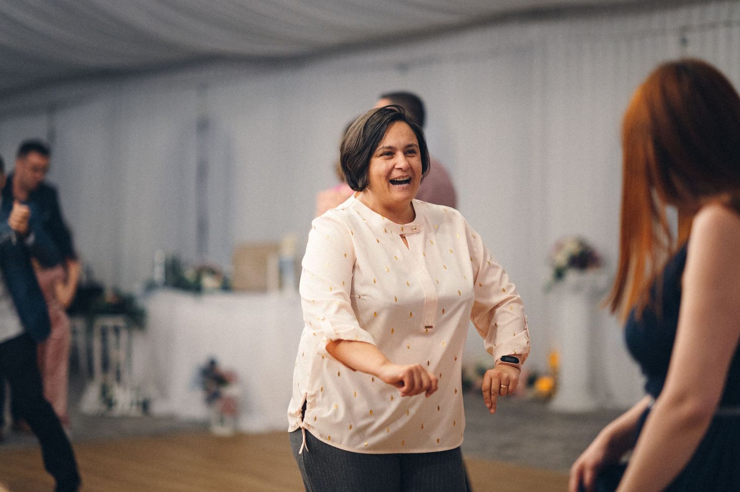 A person dancing enthusiastically at a wedding reception in a white tent.