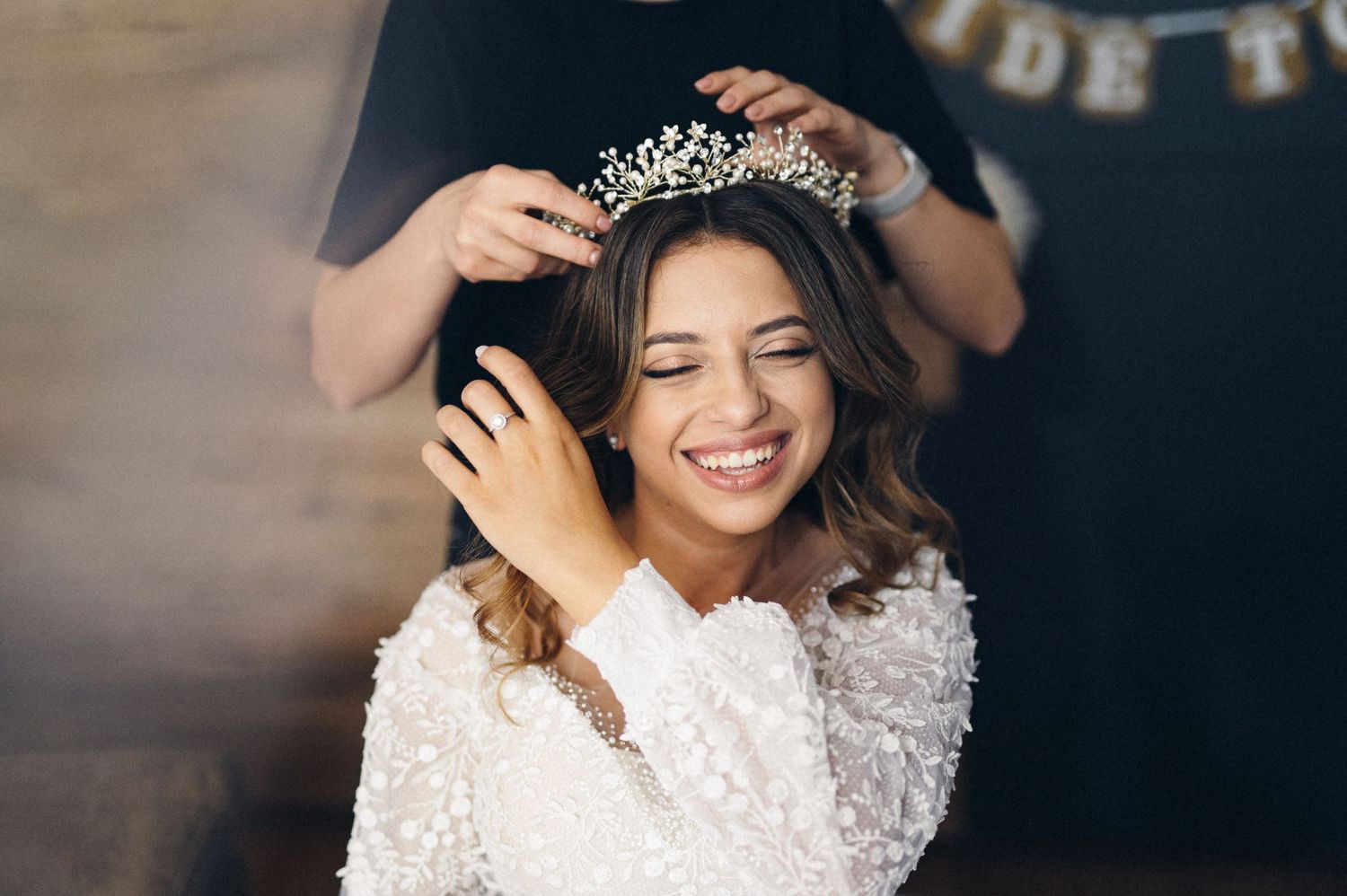 Person wearing white lace dress having a sparkly tiara placed on styled hair.