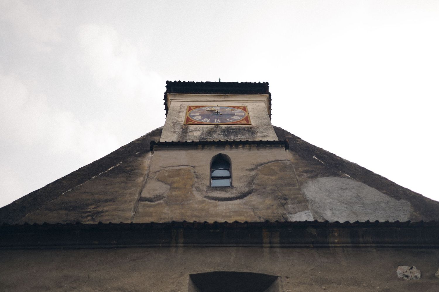 An old stone building facade with a weathered triangular pediment and small window.