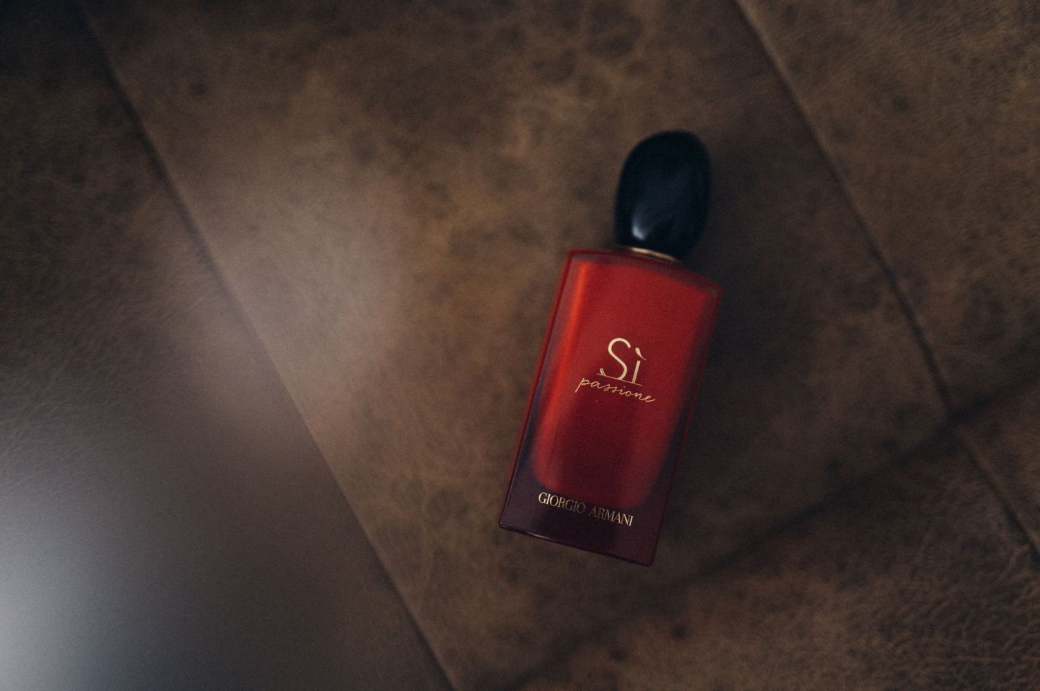 Red glass perfume bottle on dark brown surface.