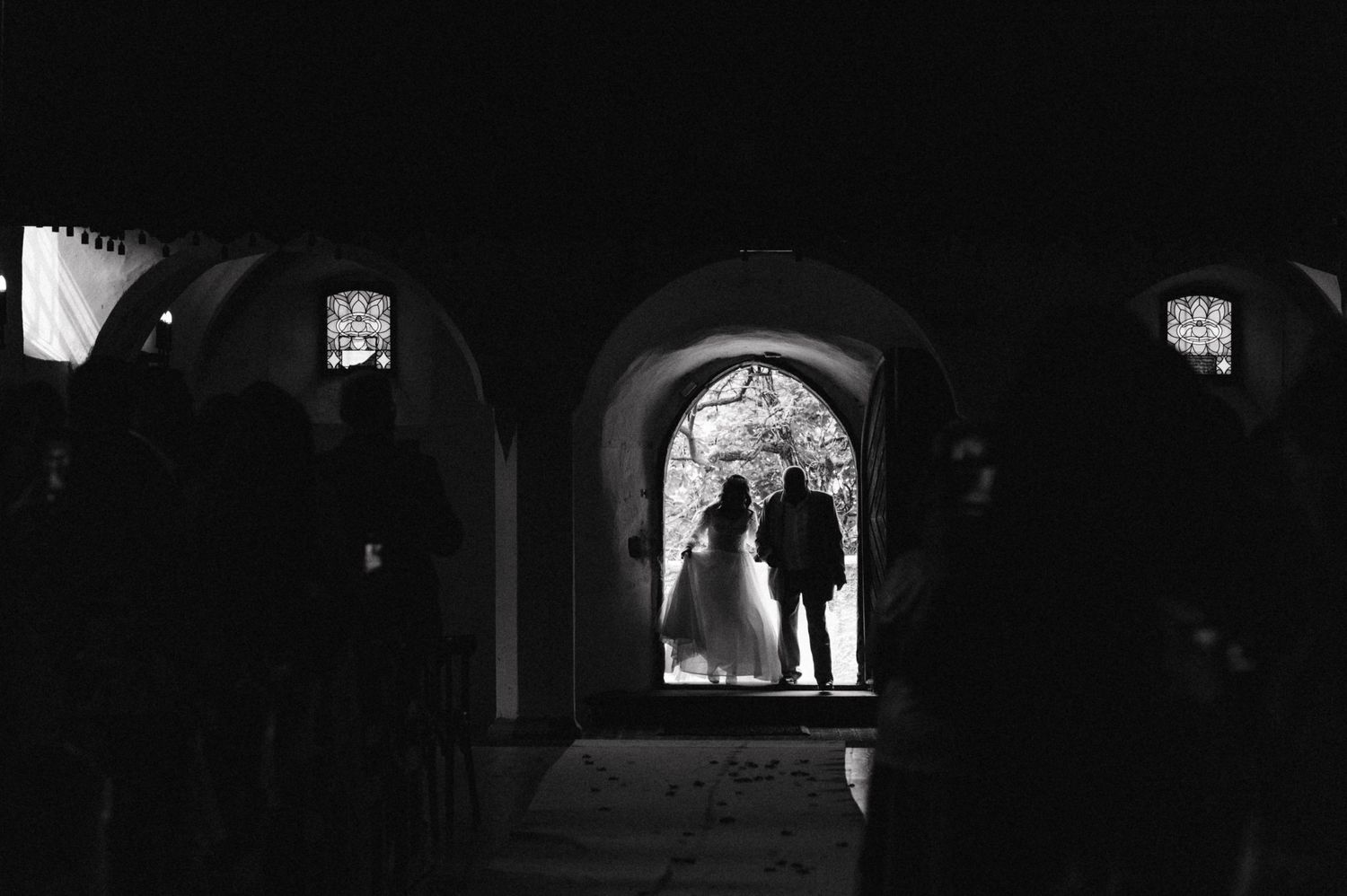 Silhouetted figures in an arched church doorway during a wedding ceremony.