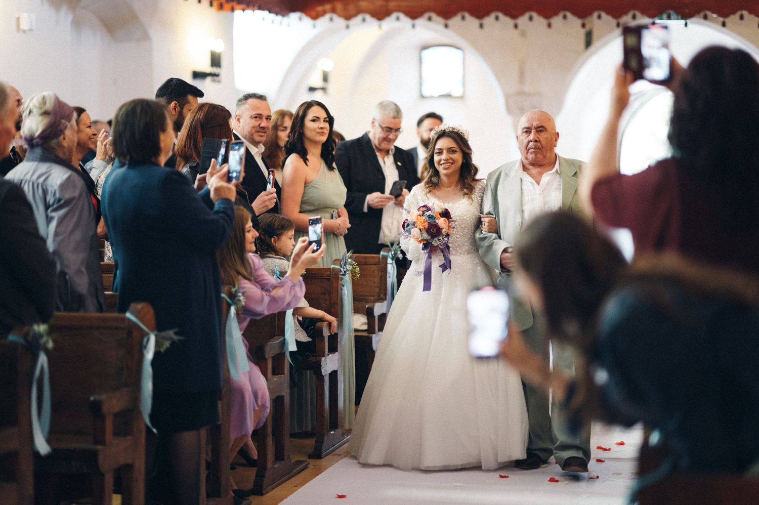 Wedding guests gather in church pews to capture photos of the ceremony.