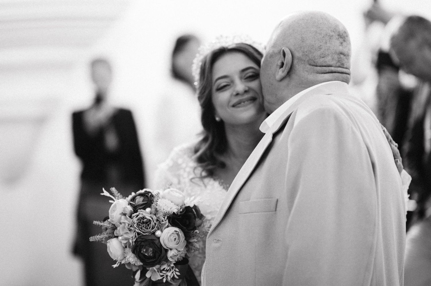 Black and white photo showing sweet emotional moment with white bouquet at wedding ceremony.