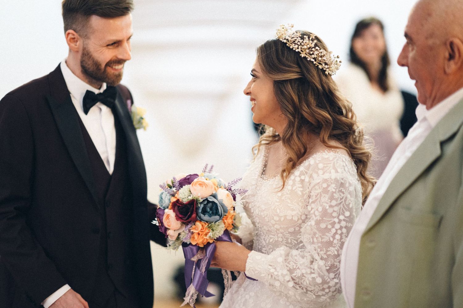 Elegant wedding ceremony with bride in lace dress holding colorful bouquet beside groom in tuxedo.