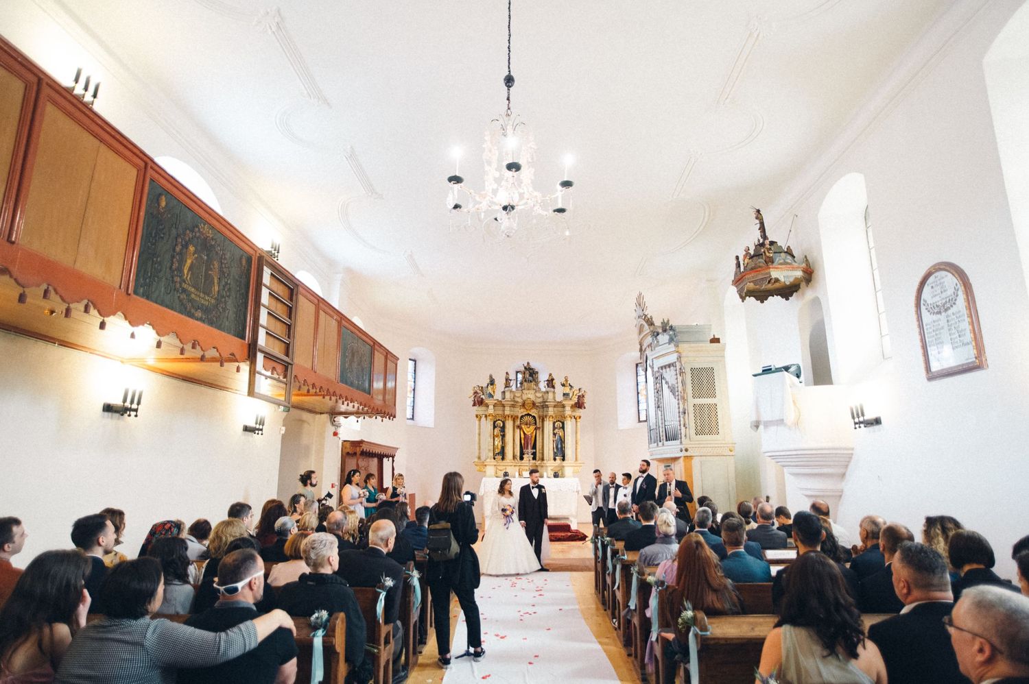 Wedding party members in formal attire watching ceremony in traditional church setting.