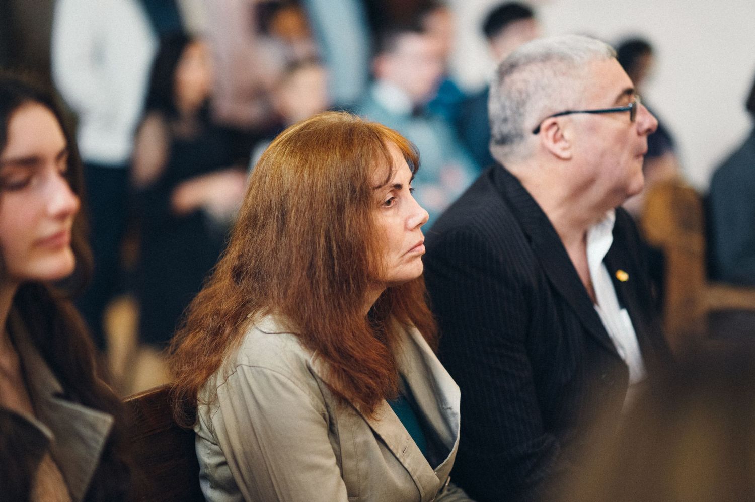 An audience sits attentively during an indoor event with focused expressions.