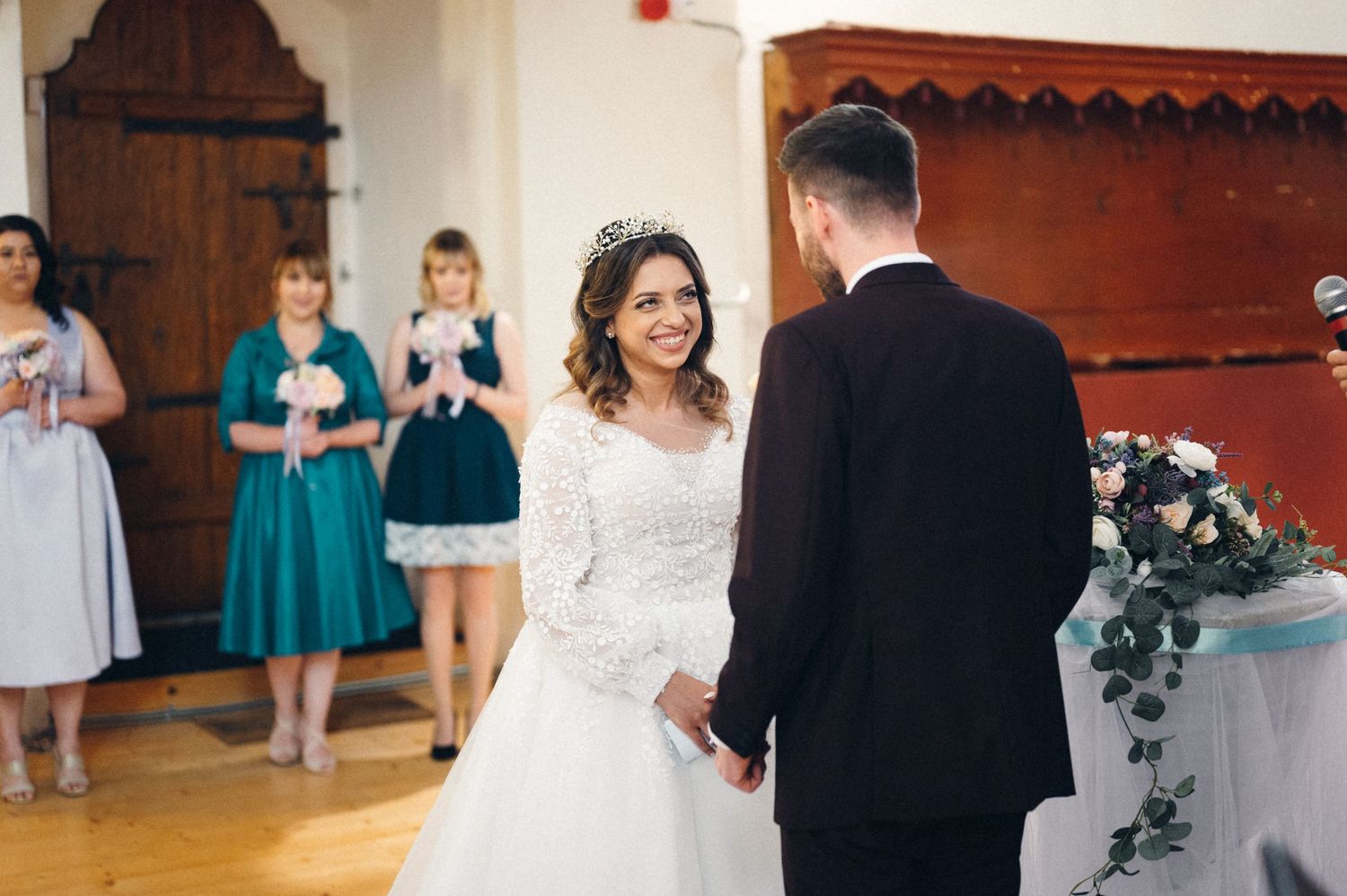 Bride and groom stand at the altar while bridesmaids in teal dresses watch from behind.