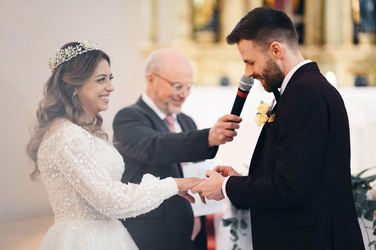 A couple exchanges vows during their wedding ceremony in a church with an officiant presiding.