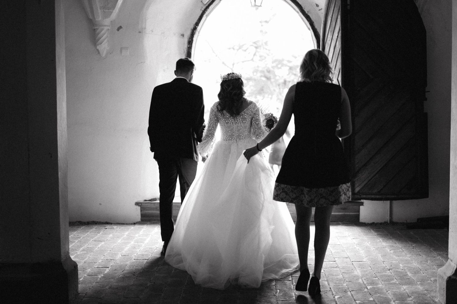 Black and white photo of three silhouettes walking through an arched church doorway.