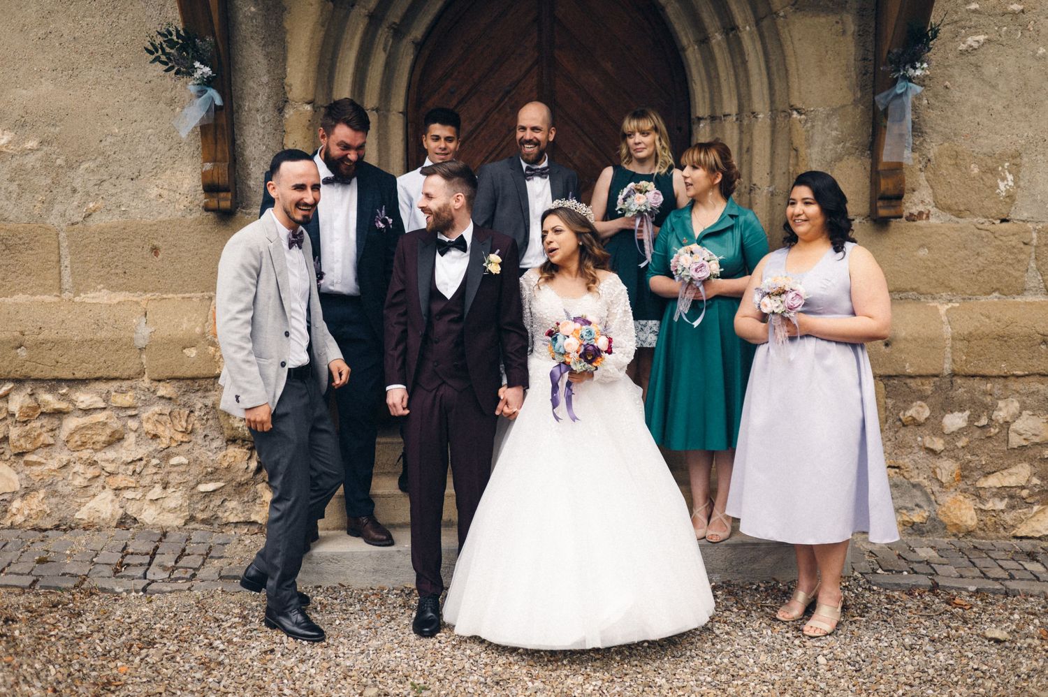 Wedding party gathered outside historic stone church entrance.