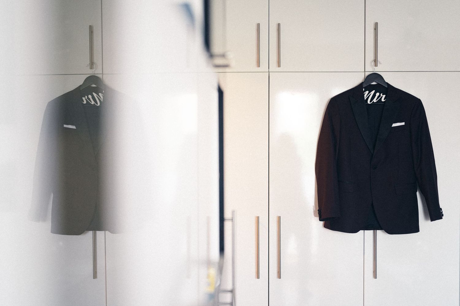 Two formal suits hanging in a minimalist white wardrobe closet.